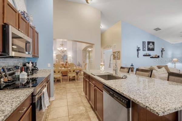 kitchen featuring light tile patterned flooring, stainless steel appliances, light stone countertops, and sink