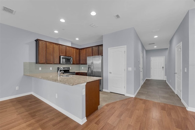 kitchen with sink, backsplash, stainless steel appliances, light stone countertops, and kitchen peninsula