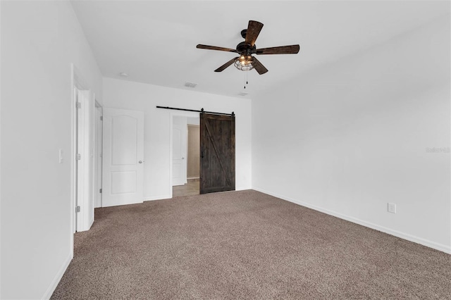 unfurnished bedroom featuring a barn door, carpet, and ceiling fan