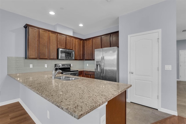 kitchen featuring light stone counters, decorative backsplash, stainless steel appliances, and kitchen peninsula