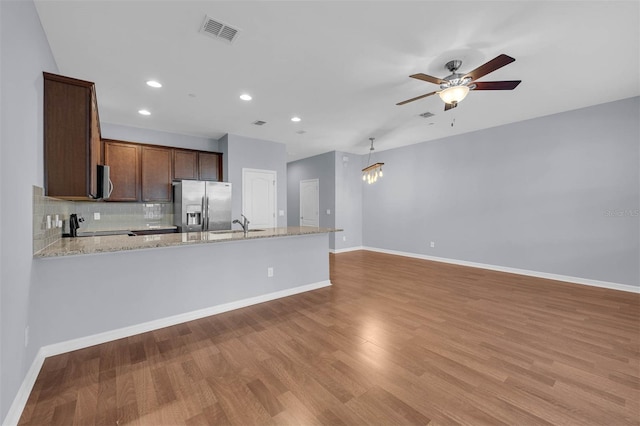 kitchen with light stone counters, light hardwood / wood-style flooring, appliances with stainless steel finishes, ceiling fan, and backsplash