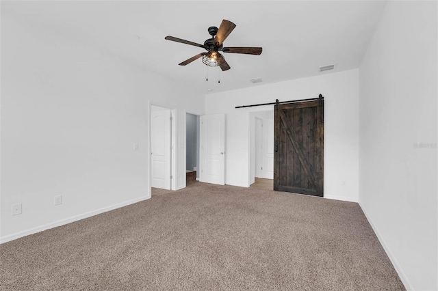 unfurnished bedroom featuring a barn door, ceiling fan, and carpet flooring