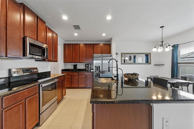 kitchen featuring sink, hanging light fixtures, stainless steel appliances, an island with sink, and dark stone counters