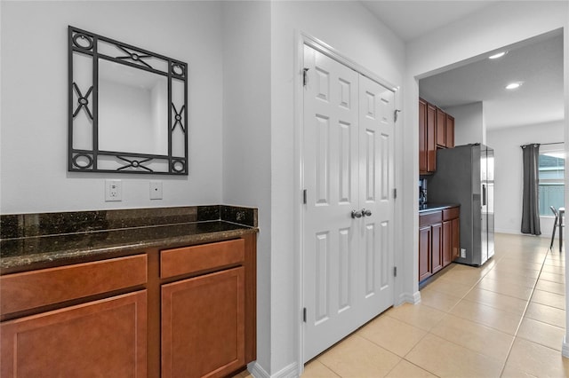 kitchen with dark stone counters, stainless steel fridge, and light tile patterned floors