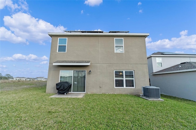 rear view of property featuring cooling unit, a lawn, and solar panels