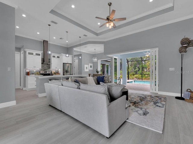 living room with a raised ceiling, ornamental molding, a high ceiling, and ceiling fan