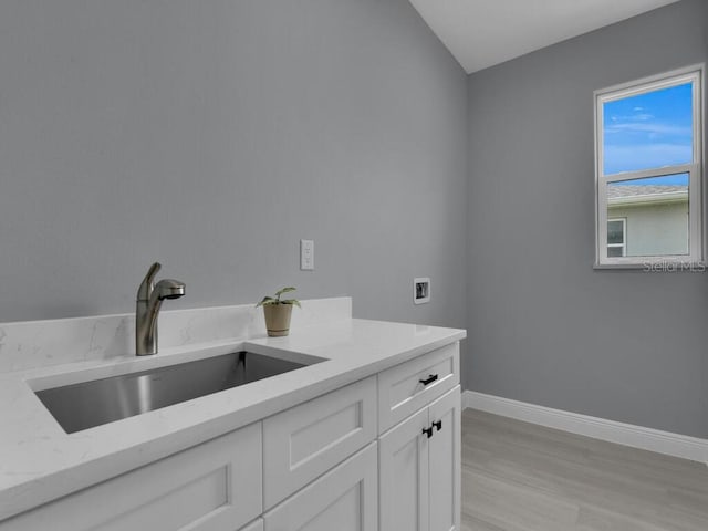 clothes washing area featuring cabinets, sink, washer hookup, and light hardwood / wood-style floors