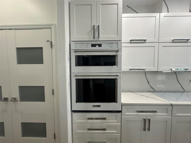 kitchen featuring white cabinetry, light stone counters, double wall oven, and decorative backsplash