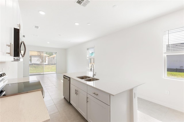 kitchen featuring sink, white cabinetry, light tile patterned floors, appliances with stainless steel finishes, and a kitchen island with sink