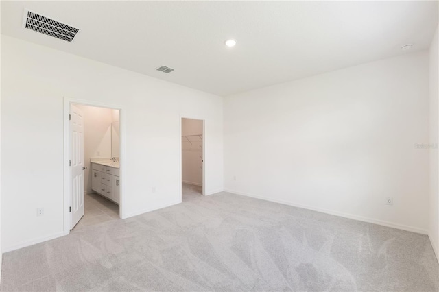 unfurnished bedroom with ensuite bath, a walk in closet, light colored carpet, and a closet