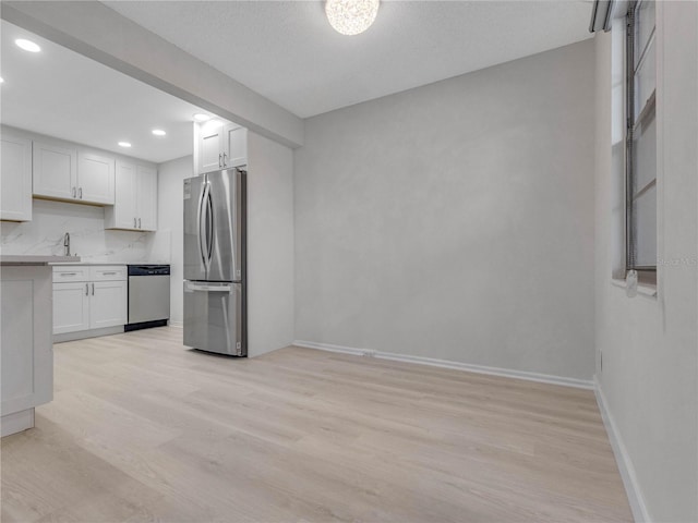 kitchen featuring sink, light wood-type flooring, white cabinets, stainless steel appliances, and backsplash