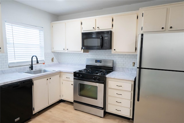 kitchen featuring sink, tasteful backsplash, white cabinetry, light hardwood / wood-style flooring, and black appliances