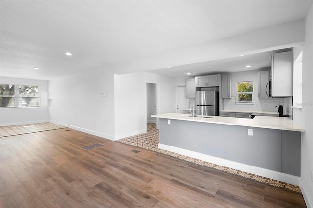 kitchen with stainless steel refrigerator, range, gray cabinetry, decorative backsplash, and kitchen peninsula