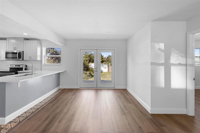 kitchen with sink, appliances with stainless steel finishes, dark hardwood / wood-style flooring, kitchen peninsula, and decorative backsplash