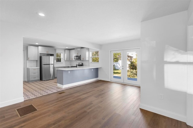 kitchen featuring backsplash, dark hardwood / wood-style flooring, kitchen peninsula, stainless steel appliances, and french doors