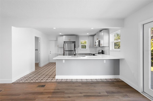 kitchen with sink, appliances with stainless steel finishes, gray cabinetry, decorative backsplash, and kitchen peninsula