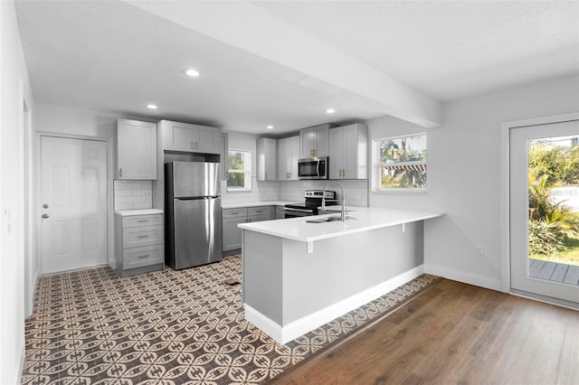 kitchen with appliances with stainless steel finishes, gray cabinetry, backsplash, a kitchen breakfast bar, and kitchen peninsula