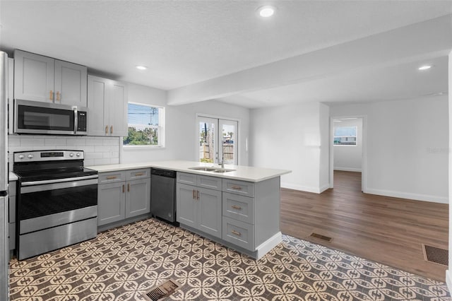 kitchen with dark wood-type flooring, gray cabinetry, appliances with stainless steel finishes, kitchen peninsula, and decorative backsplash