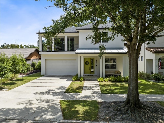 view of front facade featuring a porch, concrete driveway, stucco siding, an attached garage, and a standing seam roof