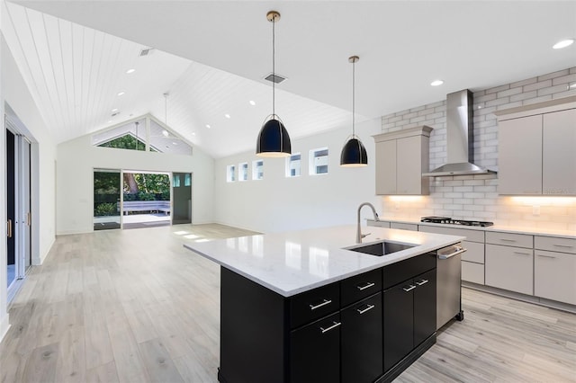 kitchen featuring sink, tasteful backsplash, a center island with sink, pendant lighting, and wall chimney range hood