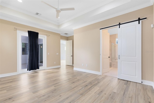 spare room featuring a barn door, ceiling fan, a tray ceiling, and light hardwood / wood-style flooring