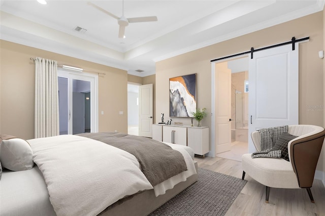 bedroom featuring ensuite bathroom, crown molding, a tray ceiling, a barn door, and light hardwood / wood-style floors