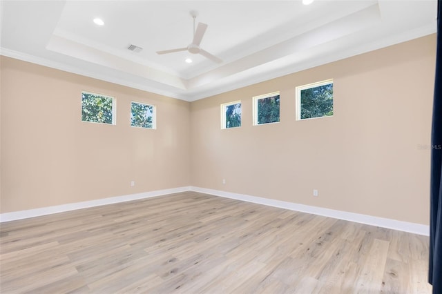 empty room featuring a raised ceiling, ceiling fan, crown molding, and light wood-type flooring