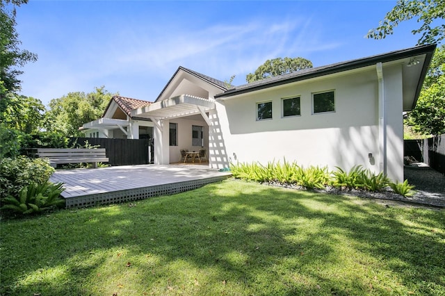 back of house featuring stucco siding, a lawn, a deck, a pergola, and fence