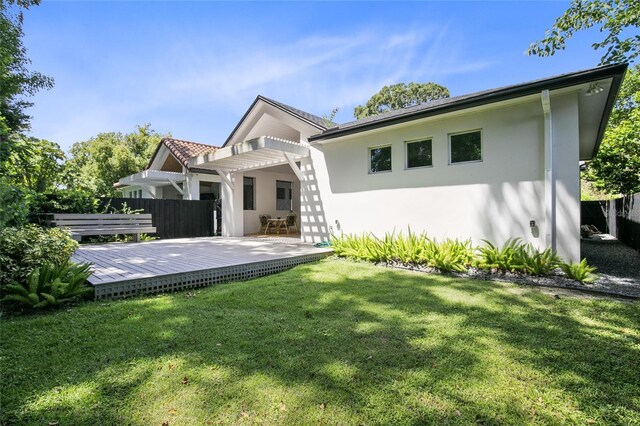 back of house with stucco siding, a pergola, a deck, fence, and a lawn
