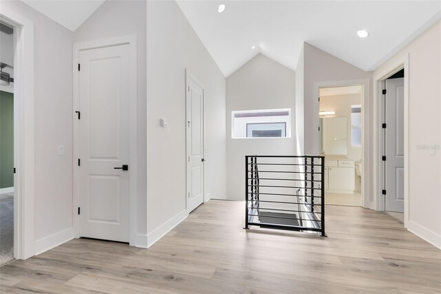 hall with an upstairs landing, vaulted ceiling, and light wood finished floors