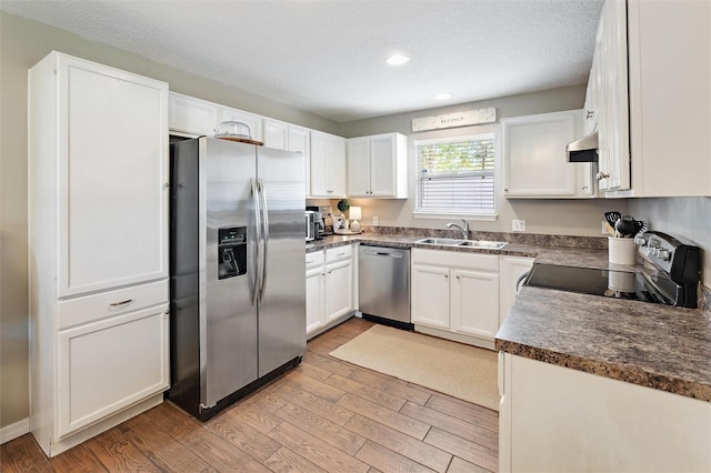 kitchen featuring sink, a textured ceiling, light wood-type flooring, appliances with stainless steel finishes, and white cabinets