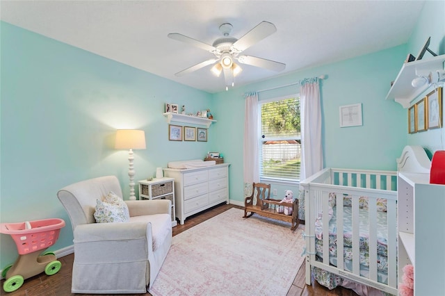 bedroom featuring a nursery area, ceiling fan, and wood-type flooring