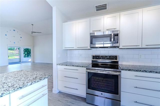 kitchen featuring white cabinetry, stainless steel appliances, light stone counters, decorative backsplash, and vaulted ceiling