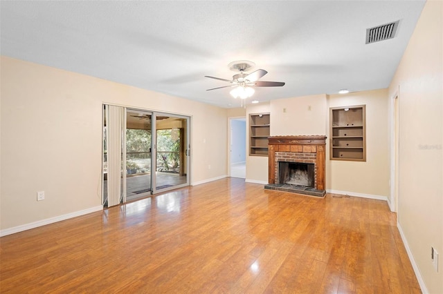 unfurnished living room with wood-type flooring, a brick fireplace, ceiling fan, and built in shelves