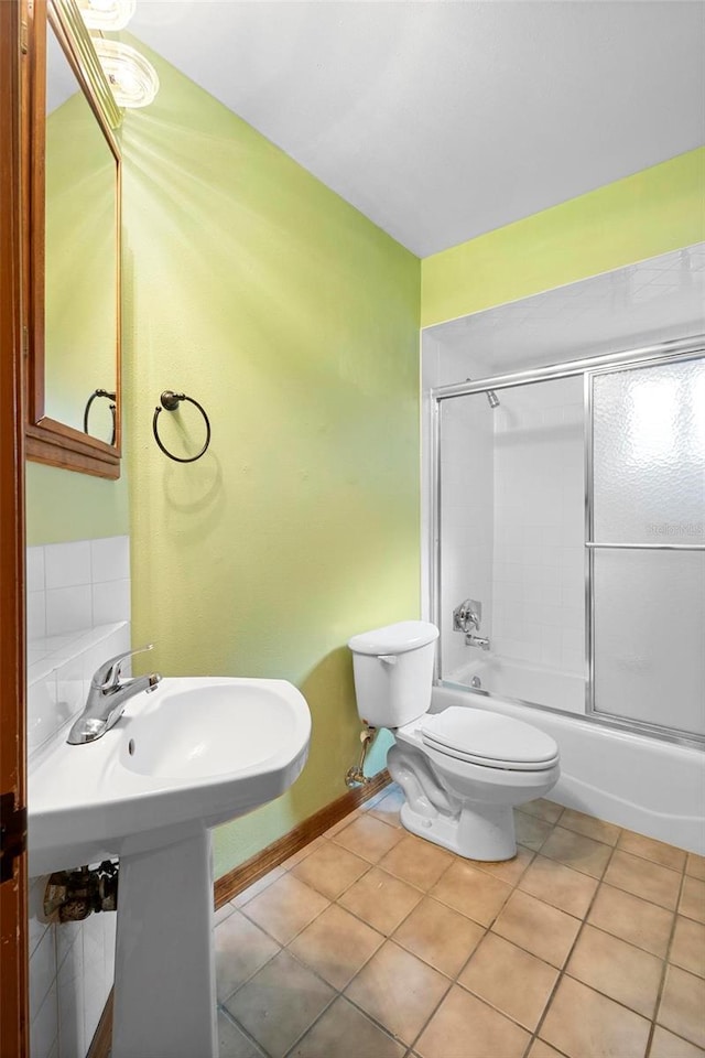 bathroom featuring tile patterned floors, toilet, and combined bath / shower with glass door