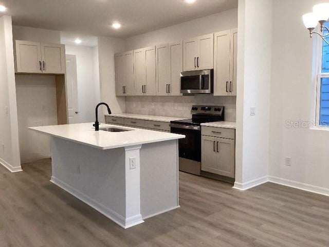 kitchen with appliances with stainless steel finishes, dark hardwood / wood-style floors, sink, backsplash, and a center island with sink