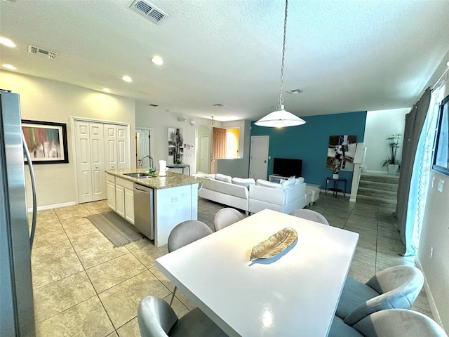 kitchen featuring sink, appliances with stainless steel finishes, a kitchen island with sink, hanging light fixtures, and white cabinets