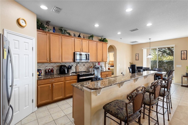 kitchen featuring pendant lighting, backsplash, a kitchen breakfast bar, dark stone counters, and stainless steel appliances