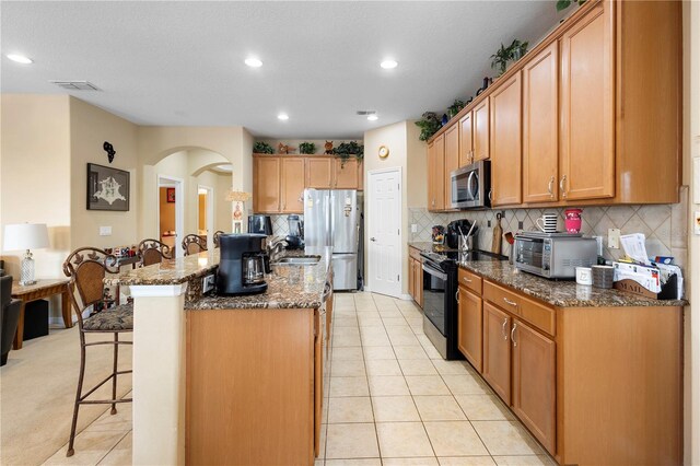 kitchen featuring stainless steel appliances, a kitchen breakfast bar, tasteful backsplash, a kitchen island, and dark stone counters