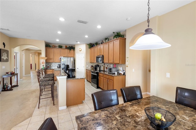 kitchen with appliances with stainless steel finishes, hanging light fixtures, a kitchen breakfast bar, tasteful backsplash, and a kitchen island