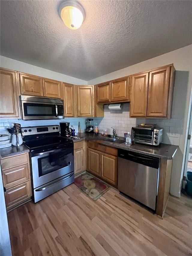 kitchen with decorative backsplash, dark countertops, light wood finished floors, and appliances with stainless steel finishes