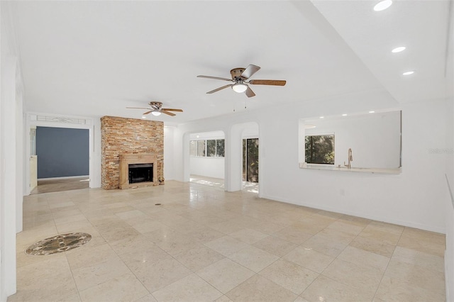 unfurnished living room featuring ceiling fan, arched walkways, a large fireplace, tile patterned floors, and baseboards