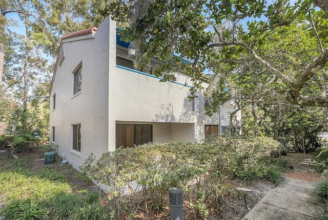 view of side of home featuring a tiled roof, stucco siding, and central AC