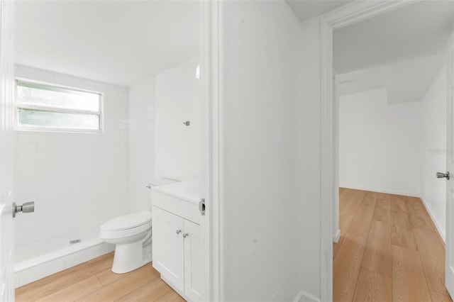 bathroom featuring vanity, toilet, hardwood / wood-style floors, and a tile shower