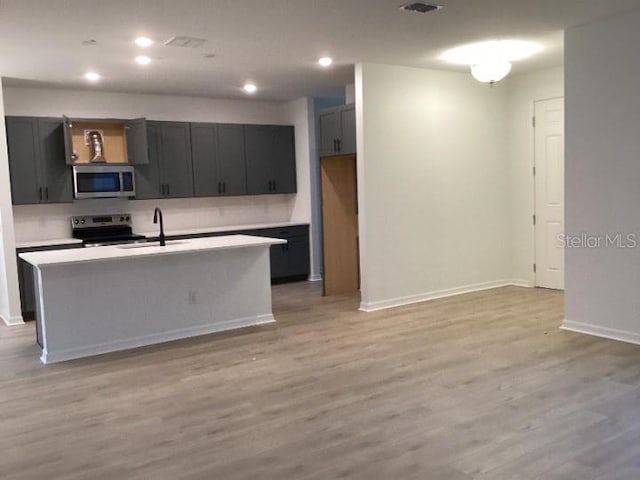 kitchen with sink, stainless steel appliances, an island with sink, and light wood-type flooring