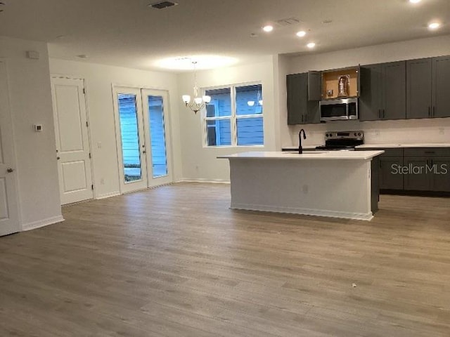 kitchen featuring decorative light fixtures, sink, light hardwood / wood-style floors, stainless steel appliances, and a center island with sink