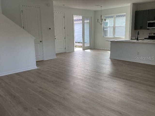 unfurnished living room featuring an inviting chandelier, light hardwood / wood-style floors, and a healthy amount of sunlight