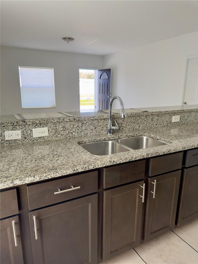 kitchen with dark brown cabinetry, sink, light tile patterned floors, and light stone counters