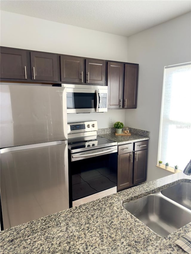 kitchen with stainless steel appliances, sink, stone counters, and dark brown cabinetry