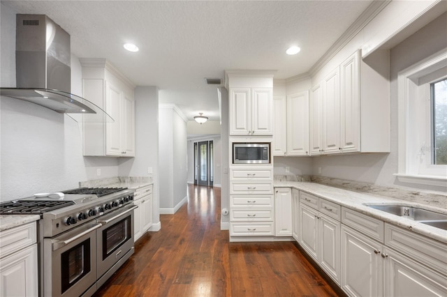 kitchen with wall chimney range hood, appliances with stainless steel finishes, white cabinetry, light stone countertops, and dark hardwood / wood-style flooring